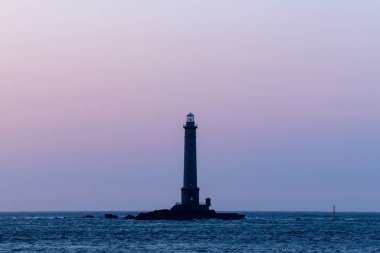 Cap de la Hague yakınlarında gün doğumunda yumuşak eğimli bir gökyüzüne karşı duran sakin denizde, kayalık bir çıkıntının üzerinde yalnız bir deniz feneri duruyor. Sakin atmosfer, yumuşak pastel renkler ve minimalist bileşimlerle güçlenir..