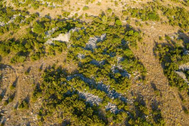 Château de Opoul Perillos yakınlarındaki güneşli bir tepenin havadan görünüşü, engebeli araziye yeşil çalılar ve ılık yaz ışığı altında ortaya çıkan taşlar eşlik ediyor..