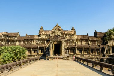 Geniş taş geçit Angkor Vat 'ın Voie Royale boyunca uzanan ve palmiye ağaçları tarafından çerçevelenen ana giriş pavyonuna çıkar ve parlak mavi bir gökyüzünün altına kurulur. Tarihi Khmer mimarisinde yıpranmış kumtaşı, süslü oymalar ve simetrik çizgiler yer almaktadır..