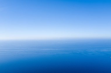 Sakin Akdeniz 'in açık mavi gökyüzü ile karşılaşmasının geniş bir görüntüsü. Yumuşak eğimler ve ince tekne izleri barışçıl, minimalist bir atmosfer yaratıyor..