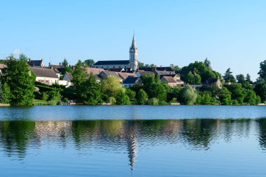Dampierre en Burly 'nin çatısından yükselen çarpıcı bir kilise kulesi, bereketli ağaçlar ve berrak yaz gökyüzünün altında sakin bir göletin sularında yansıtılan geleneksel köy evleri..