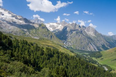 Bereketli kozalaklı ormanlar dramatik kayalık dağların altındaki yuvarlanan tepeleri ve parlak mavi bir gökyüzünün altındaki kar parçalarını kaplıyor. Dağılmış bulutlar Vallee de lA Neuve, İsviçre 'de.