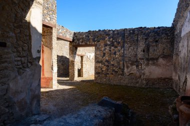 Antik volkanik taş ve alçı duvarlar İtalya 'nın Pompeii kentindeki arkeolojik kamaralarda bir dizi açık kapı oluşturur. Kıtır güneş ışığı pürüzlü dokuları, solmuş kırmızı boyaları ve berrak mavi gökyüzünün altında yıpranmış duvarları ortaya çıkarır..