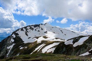 Eriyen kar örtüleri Aiguillette des Houches 'in engebeli yamaçlarında güneş ışığı dağılmış bulutların arasından kırılıyor ve desenli dağ manzarasını aydınlatıyor..