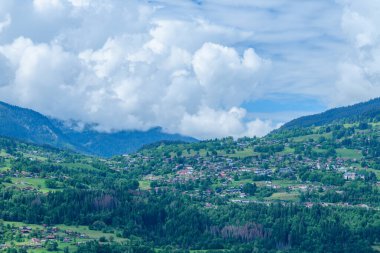 Büyüleyici dağ köyü Combloux çevresi gür ormanlar ve yükselen kümülüs bulutlarının altında yuvarlanan tepelerle ve parlak mavi gökyüzüyle çevrili..