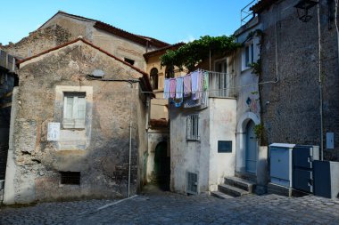 Sessiz bir Maratea caddesinde yıpranmış taş binalar arasında renkli çamaşırhaneler asılı duruyor. Dokulu cepheler, kaldırım taşları ve yumuşak gün ışığı Akdeniz 'de yaşanabilir bir atmosfer yaratır..