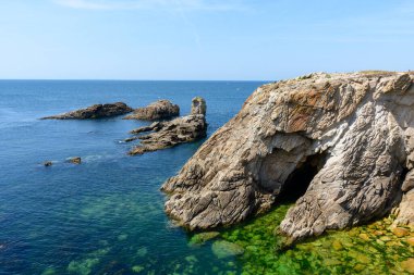 Karanlık deniz mağarası olan büyük kayalık kayalıklar Pointe Beg-An-Aud 'da açık yeşil-mavi suyla karşılaşıyor. Kalıplı taş ve su altındaki kayalar parlak güneş ışığı altında görülebiliyor..