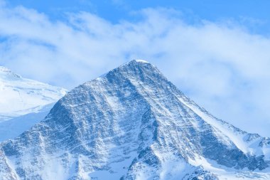 Aiguille du Gouter kıtır kıtır kar ve engebeli kaya dokularıyla Fransız Alpleri 'ndeki yumuşak bulutlar ve canlı mavi gökyüzüne karşı yükselir..