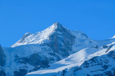 Mont Maudit, Fransız Alpleri 'ndeki parlak mavi gökyüzünün altında parlak güneş ışığıyla aydınlatılan keskin, karla kaplı tepeleri ve parlayan buzla dimdik ayakta duruyor..