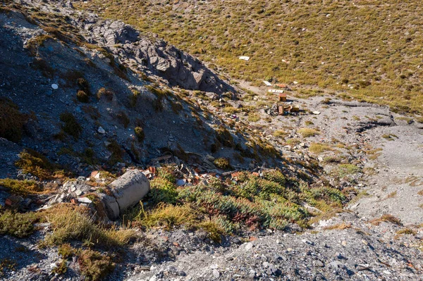 Kırık beton, tuğla ve çeşitli atık yığınları Arjantin, Sardunya yakınlarındaki seyrek bitki örtüsüne sahip kuru ve kayalık bir yamaçta bulunur. Sert güneş ışığı engebeli araziyi ve çevresel etkiyi vurguluyor.