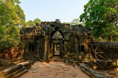 Ta Som tapınağının yıpranmış taş girişi Kamboçya Angkor bölgesinde yoğun yeşil ağaçların arasında duruyor. Karmaşık bas-rahatlatıcı ve yaşlı duvar ustaları yumuşak öğleden sonra güneş ışığıyla vurgulanarak sakin bir tarihi atmosfer yaratırlar..