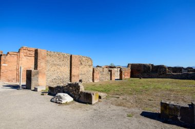 Comitium 'un antik taş ve tuğla duvarları İtalya' nın Pompeii kentindeki açık bir arkeolojik alanda duruyor. Parlak güneş ışığı, canlı mavi gökyüzüne karşı desenli taş ve dağınık parçalar ortaya çıkarıyor..