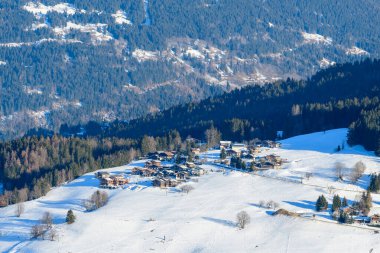 Megeve yakınlarında, sık yeşil ormanlar ve yuvarlanan dağ arazisiyle çevrili, güneşli, kar örtülü bir yamaçta bir grup geleneksel alp chalet yuva kurar..
