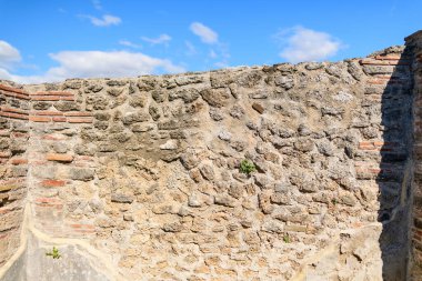 Antik taş ve tuğla bir duvar yakın görüntüsü kaba dokular, dağınık bulutlar ile canlı mavi bir gökyüzü karşı kurulmuş. Tarihi taş ustası, çatlaklardaki yikim ve ince bitki gelisimi katmanlarini ortaya çikariyor..