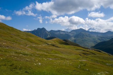 Geniş yeşil vadi, kaygan tepeleri ve engebeli bir patikası olan engebeli tepeler ve Val dAoste Alpleri 'ndeki dağınık bulutlarla dolu bir gökyüzü..