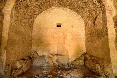 Yıpranmış taş duvarlar ve kubbeli tavan Pompeii 'deki banliyö hamamlarının bu iç manzarasını tanımlar. Uzay, arkeolojik detayları vurgulayan desenli alçı, soluk geometrik desenler ve yumuşak, doğal ışık özelliklerine sahiptir..