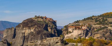 İki tarihi manastır, Büyük Meteor ve Varlaam, Yunanistan 'ın Meteora kentindeki yüksek kumtaşı oluşumlarının tepesinde, sonbahar yaprakları ve açık mavi gökyüzüyle çevrili olarak duruyorlar..