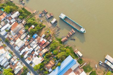 Teneke çatılı evler ve Vietnam 'daki Chau Doc' taki çamurlu nehir kıyısı boyunca yüzen yapılar. Görüntü, demirlemiş tekneler, yeşil bitki örtüsü ve Mekong Delta yerleşim yerinin planlarını içeriyor..