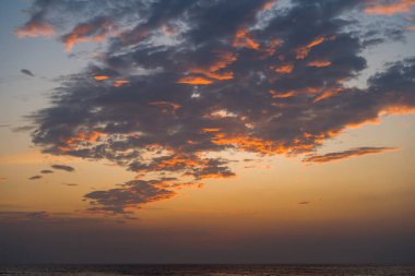 Büyük kara bulutlar, Kovalam Grove Plajı 'ndaki sakin denizin üzerinde akşam gökyüzünde alev alev yanan turuncu ışığı yakalıyor. Dramatik günbatımı sıcak ve atmosferik bir kıyı manzarası yaratır..