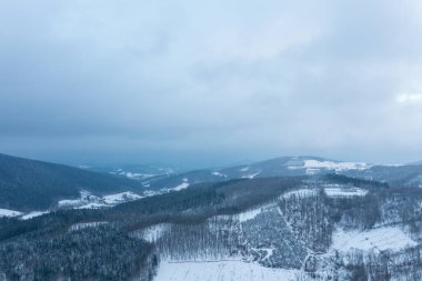 Morvan bölgesindeki karla kaplı tepelerin ve yamalı ormanların karamsar, bulutlu bir gökyüzü altında geniş bir manzarası var. İnce mavi tonlar ve yumuşak ışık sakin, kış manzarası yaratır..