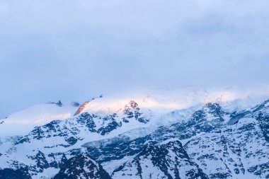 Sabah güneşi, Mont Blanc 'ın üst yamacında soluk, bulutlu gökyüzünün altında taze kar ve dramatik dokuları aydınlatarak otluyor..