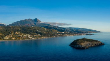 Calabrian sahili açıklarındaki Isola di Cirella 'nın hava manzarası. Sakin mavi sular, yeşil bir ada ve gün doğumunda berrak bir gökyüzünün altındaki uzak dağlar..