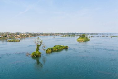 Laos 'un güneyindeki 4000 ada bölgesindeki Mekong Nehri' nin geniş mavi sularından yayılan yeşil adacıklar ortaya çıkar. Açık gün ışığı ve ağaçlarla kaplı uzak bir nehir kıyısı geniş ve sakin bir manzara yaratır..