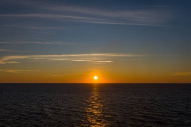 Sıcak altın güneş ışığı, ufukta güneş batarken sakin sularda yansıyarak Adriyatik ve İyon denizleri arasında sakin bir deniz manzarası oluşturur. İnce bulutlar ve eğimli bir gökyüzü barışçıl ve minimal atmosferi arttırır..