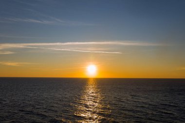 Güneş, sakin İyon Denizi 'nin üzerinde alçalır. Nazik dalgalar üzerinde parlak bir altın yansıma oluşturur. İnce bulut çizgileri ve eğimli bir gökyüzü sakin ve minimal bir deniz manzarası yaratır..