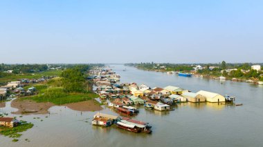 Vietnam 'ın Chau Doc kenti yakınlarındaki nehirde yüzen bir köye ait hava perspektifi, su boyunca demirlemiş renkli evler ve botlar. Sahnede yemyeşil bankalar, açık gökyüzü ve nehir kenarındaki yerleşim yerlerinin eşsiz mimarisi yer alıyor.