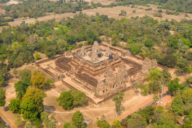 Kamboçya Angkor bölgesindeki kurak tarlalar, dağınık ağaçlar ve kırsal alanlarla çevrili Pre Rup tapınağının açısal yapısını gösteren hava manzarası. Antik kumtaşı anıtı berrak gökyüzünün altında kırsal bir parçanın ortasında duruyor..