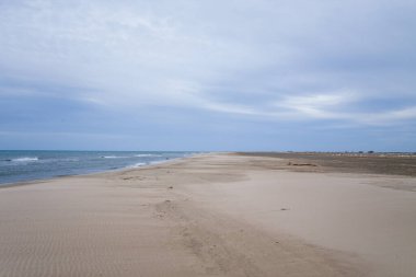 Fransa 'nın Saint Louis du Rhone Limanı' ndaki Plage Napolyon 'un geniş bir manzarası, el değmemiş kum, sakin dalgalar ve uçsuz bucaksız bulutlarla dolu bir gökyüzü. Açık arazi huzurlu ve geniş bir kıyı atmosferi yaratır..