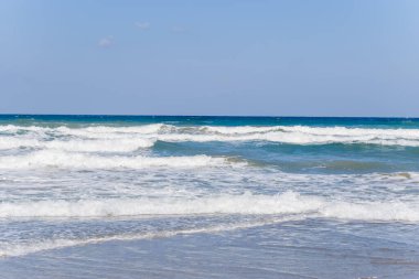 Yumuşak dalgalar Girit 'in Georgioupolis sahilinin sığ kıyılarında bulutsuz bir gökyüzünün altında ışıldayan turkuaz suyla akıyor. Sakin deniz manzarası bir sakinlik ve açıklık hissi uyandırıyor..