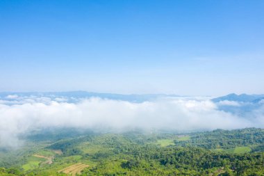 Dien Bien, Vietnam 'daki yemyeşil tepeler ve orman vadileri üzerinde yumuşak beyaz bulutlar sürükleniyor. Açık mavi gökyüzü ve uzak dağ sırtları sakin ve geniş bir manzara yaratır..