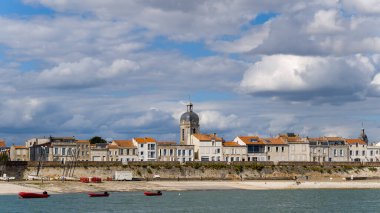 Turuncu kiremitli çatıları olan klasik taş binalar La Rochelle, Charente-Maritime 'in rıhtımında eski kasabanın üzerinde yükselen belirgin kuleye sahiptir. Sahnede desenli bulutlar, kumlu plaj ve sakin Atlantik suları yer alıyor.