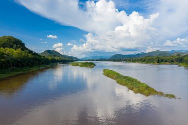 Luang Prabang, Laos yakınlarındaki Mekong Nehri 'nin çimenli adaları ve yemyeşil bankaları geniş görüşlü. Yükselen kümülüs bulutları ve mavi gökyüzü uzak orman dağları tarafından çerçevelenmiş sakin suda yansıtılır..