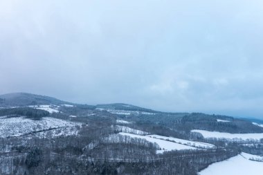 Morvan bölgesindeki yuvarlanan tepeler ve karla kaplı ormanlar geniş görüş alanımızda. Yumuşak mavi kış ışığı ve bulutlu gökyüzü sakin ve uzak bir atmosfer yaratır..