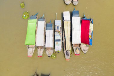 Yukarıdan bakıldığında, Can Tho, Mekong Delta, Vietnam 'daki Cai Rang yüzer pazarında yan yana demirlemiş bir dizi kapalı pazar teknesi görülüyor. Yeşil, beyaz ve kırmızı renkli ayırt edici brandalar çarpıcı bir geometrik desen oluşturur.