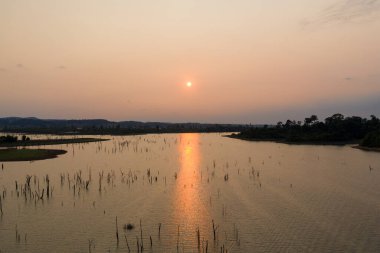 Altın akşam ışığı Nakai Gölü 'nün sakin suları boyunca yankılanır, sel basmış manzaradan ağaç kütükleri yükselir ve ufuk boyunca uzanan uzak tepeler. Sakin rezervuar sahnesi, berrak bir gökyüzünün altında yumuşak ve ılık tonlarda yıkanır..