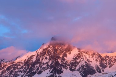 Karanlık menekşe ve pembe bulutlar Aiguille du Midi 'nin karla kaplı, pürüzlü armasında ilerlerken alacakaranlık ışığı Fransız Alpleri' ndeki dramatik kaya dokusunu vurguluyor..