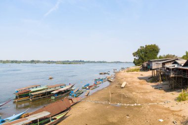 Güney Laos 'un 4000 ada bölgesindeki Mekong Nehri' ndeki kırsal yapışkan evlerin yanındaki kumlu kıyıda uzun ahşap kayıklar hizaya gelir. Parlak gün ışığı, sakin suyu, dağılmış tekneleri ve sakin nehir kenarındaki köy atmosferini gözler önüne seriyor..