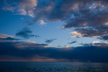 Adriyatik Denizi 'nin altında sakin bir deniz manzarası alacakaranlıkta katmanlı mavi ve gri bulutlarla dolu dramatik bir gökyüzü. İnce renk değişimleri ve yumuşak akşam ışığı barışçıl ve açık bir ufuk yaratır..