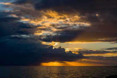 Adriyatik Denizi 'nin üzerinde kara fırtına bulutları toplanırken altın güneş ışığı su üzerinde dramatik ışınlar ve canlı yansımalar yaratıyor. Aydınlatılmış gökyüzü ve gölgeli okyanus arasındaki çarpıcı zıtlık alacakaranlıkta cesur bir kıyı manzarası yaratır..