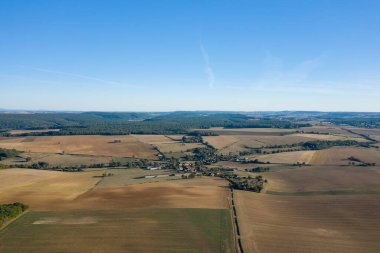 Havadan bakıldığında, Fransa 'nın orta kesimindeki açık mavi gökyüzünün altında geniş altın tarlalar ve uzak ormanlık alanlarla çevrili küçük bir kırsal köy görülüyor. Açık arazi ve geometrik desenler sakin ve ferah bir hissi uyandırıyor..