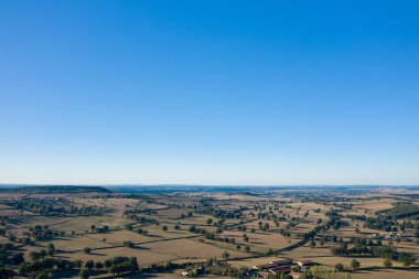 Güneşli kırsal manzaranın geniş hava manzarasında altın tarlalar, dağınık ağaçlar ve Cuncy les Varzy yakınlarındaki uçsuz bucaksız mavi gökyüzünün altındaki uzak tepeler mozaiklenir. Açık tarım arazisi ve geometrik alan desenleri bir boşluk hissi uyandırıyor.