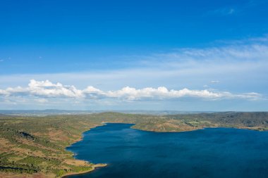 Derin mavi su, yuvarlanan yeşil tepeler ve güneşli bir günde dağınık bulutlarla dolu geniş bir gökyüzü içeren Salagou Gölü 'nün havası..