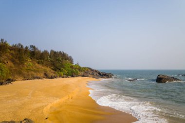 Geniş altın kum plajı, Hindistan 'ın Bekal kıyı şeridi boyunca yumuşak dalgalarla ve engebeli kayalarla buluşur. Sıcak güneş ışığı doğal dokuları ve barışçıl atmosferi vurgular..