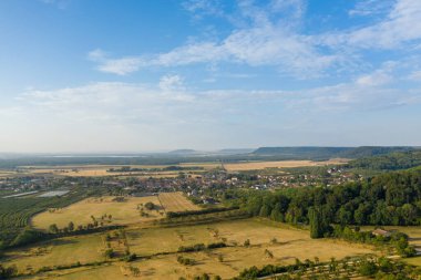 Hattonchatel köyünün geniş hava manzarası altın tarlalar, meyve bahçeleri ve parlak mavi gökyüzünün altındaki yoğun yeşil ormanlarla çevrilidir. Kompozisyonda Lorraine bölgesinin yama alanları, kırsal yerleşim alanları ve kayan tepeleri vurgulanıyor..