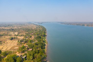 Stoeng Treng, Kamboçya yakınlarındaki Mekong Nehri 'nin geniş bir hava perspektifi, sakin mavi suları çevreleyen tarlalar, dağınık evler ve yemyeşil alanlar. Nehir kenarı köyü ve tarım arazisi sakin ve açık bir arazi oluşturur.