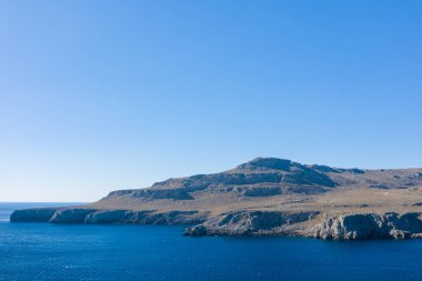Girit 'in Kato Zakros kenti yakınlarındaki derin mavi Akdeniz sularının üzerinde engebeli, güneşli bir burun yükseliyor. Kurak arazi ve geniş açık gökyüzü bir açıklık ve sadelik hissi yaratır..